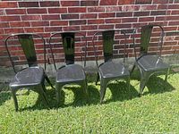 Front view of four black metal bistro chairs on grass against brick wall