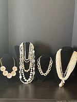 Group shot of multiple white necklaces on four display busts