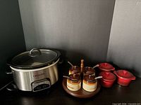 Overall lot showing slow cooker, four condiment jars on lazy Susan, and two red mini cocottes