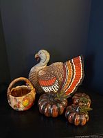 Group shot showing fabric turkey pillow, ceramic turkey basket and three ceramic pumpkins