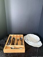 Flatware in wooden drawer beside china bowls and platter