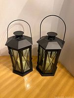 Two black metal lanterns with glass panels and ivory flameless candles inside