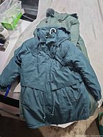 Both parkas laid out: green long parka underneath, teal shorter parka on top