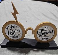 Front view of gold spectacles figurine with quote on lenses, lightning bolt accent, black base