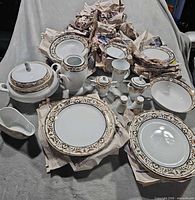 Overview of stacked plates, bowls and serving pieces with gold scroll trim
