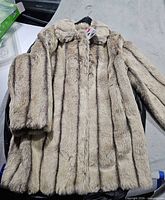 Front view of full-length beige striped faux fur coat on hanger with tag