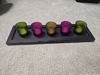 Front view of black tray with five coloured votive holders