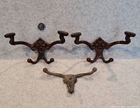 Two ornate cast iron hooks and one bronze steer hook shown together for scale
