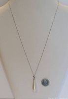 Full view of silver chain necklace with pearl drop next to coin for scale