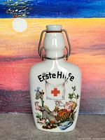 Front view of porcelain Erste Hilfe cognac flask showing graphic and stopper