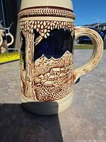 Left side of stein showing alpine village scene, handle visible