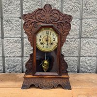 Full view of carved wood New Haven gingerbread mantel clock on table
