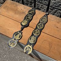 Both leather straps laid out showing overall length and brass motifs