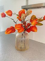 Ribbed glass vase holding artificial orange Chinese lantern stems with leaves
