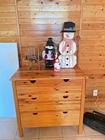 All four items together on dresser: wooden snowman, plush snowman, small snowman figurine, glass/metal lantern