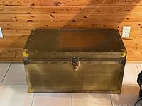 Front view of brass-finish metal trunk with latch and corner protectors