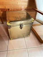 Front view of brass-toned metal trunk with latch and riveted edges
