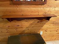Front view of shelf mounted on pine wall showing scalloped brackets and overall design