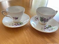 Two teacups with matching saucers showing front view, floral design and gold trim