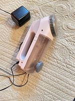 Windmere fabric shaver lying on surface with AC adapter attached