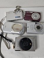 Front view of all five cameras showing brands, lens covers, finishes