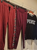 Three garments hanging: burgundy sweatpants, burgundy leggings, black sweatshirt