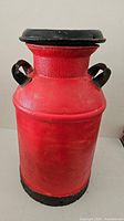 Full view of red metal dairy milk can, lid on, handles visible