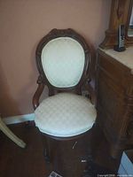 Front view of carved wood chair with cream upholstery and casters