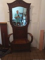Full view of tall carved hall seat with mirror, coat hooks, armrests and storage bench