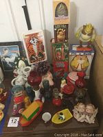 Wider view of lot items including clown bank, musical monkey box, oil lamps, and various figurines on table