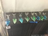 Eight glass dolphins displayed on a black shelf, showing variation in colors including blue, green, and aqua shades, all with clear glass tails and rounded bodies.