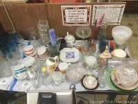 Wide view of the lot with assorted glassware, cups, vases, plates and other items spread out on a table