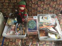 View of lot contents showing plush doll, plastic toy crib with two baby dolls, box of cards and stamps, and assorted toys in plastic bins