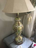 Full view of the ceramic table lamp showing decorative base, wooden platform, and beige fabric lampshade.