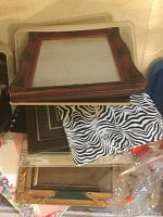 Stack of assorted photo frames including a reddish-brown decorative frame, zebra print frame, and others with various patterns.