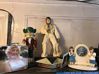 Full view including Elvis Presley figurine, Marilyn Monroe photo frame, wooden nutcracker figurine with green helmet, praying boy and girl figurines beside religious clock.