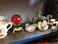 Shelf with unicorn figurines, swan figurines, red rose glass dome and ceramic mustache mug.