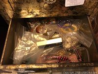 Open drawer of accessory cabinet showing assorted costume jewelry in various plastic bags including bracelets, necklaces, earrings, and brooches.