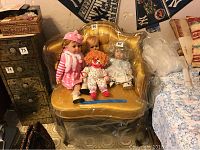 Full front view of antique wooden framed chair with gold upholstery, holding four dolls.