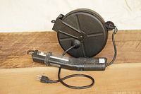 Front view of black retractable cord reel with attached work light and cord visible