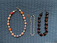 Three necklaces laid out: multicolour faux pearl, grey choker, dark brown and orange bead