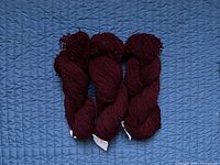 Three skeins dark maroon yarn on blue background