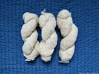 Three skeins of natural white wool yarn displayed on blue surface
