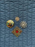 Front view of three brooches with coin for scale