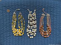 Three multi-strand bead necklaces in yellow, cream and pink displayed with coin for scale
