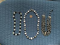 All three necklaces laid flat on blue quilted surface
