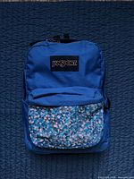 Front view of blue JanSport backpack showing painted front pocket and logo patch