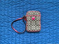 Front view of Coach wristlet displaying monogram canvas, pink trim, wrist strap