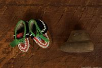 Top view of both moccasins beside clay pipe showing size and decoration