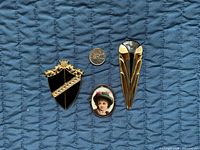 Front view of three brooches with coin for scale: shield, portrait oval, elongated teardrop